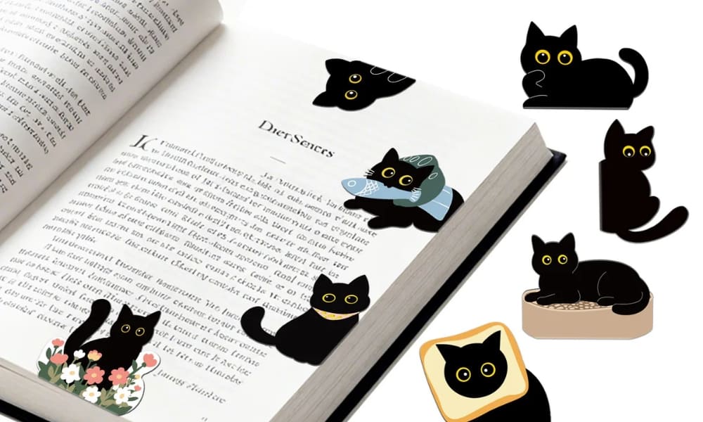 A collection of cute black cat bookmarks with large yellow eyes in various funny poses, including a cat with a fish, a cat in flowers, and a cat wearing a slice of toast. Several bookmarks are shown clipped onto the pages of an open book. Perfect kawaii stationery for cat lovers.