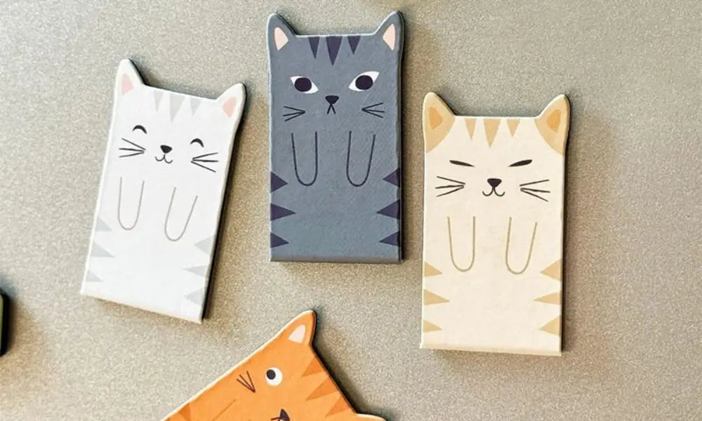 A set of four cute magnetic cat bookmarks in different colors: white, grey, cream, and ginger tabby. These feline-shaped page clips feature minimalist cartoon faces and tiny paws, ideal for marking pages in books, planners, or journals.