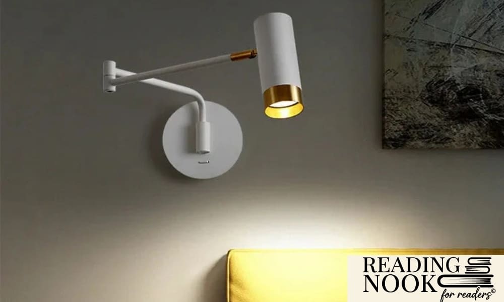 A modern articulating wall sconce by Reading Nook in matte white with gold brass accents. The swing arm lamp is mounted on a grey wall, providing warm directional light over a bright yellow headboard. Sleek minimalist bedside lighting for a contemporary bedroom