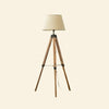 A rustic wooden tripod floor lamp with a beige fabric shade and black metal accents.